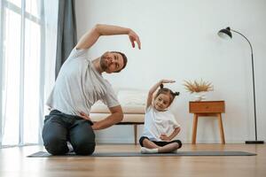 Spine exercise... Father with little daughter are doing yoga at home photo
