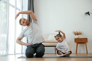 Front, view, together... Father with little daughter are doing yoga at home photo