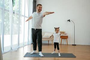 Front ,,view, together. Father with little daughter are doing yoga at home photo