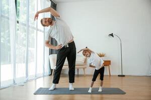 Spine exercise. Father, with little daughter are doing yoga at home photo