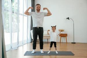 Front, view, together. Father with little daughter are doing yoga at home photo