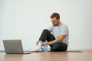 Man is, sitting on the yoga mat with laptop on the floor photo