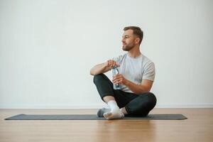 Taking,, a break, with bottle of water. Yoga man is sitting on a mat at home photo