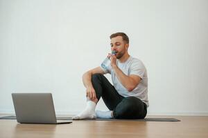 Man, is, sitting on the yoga mat with laptop on the floor photo