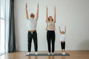 Warm up exercises. Family ,,of mother, father and daughter are doing yoga at home photo