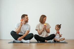 With apples in hands. Family ,of ,mother, father and daughter are doing yoga at home photo