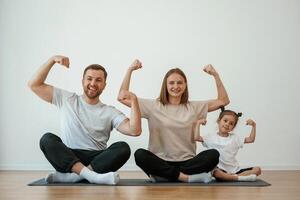 Showing the biceps,, strong. Family of mother, father and daughter are doing yoga at home photo