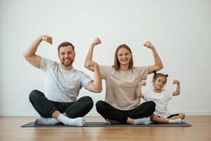 Showing, the biceps, strong. Family ,of mother, father and daughter are doing yoga at home photo