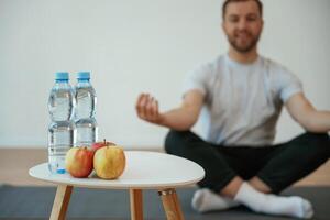 Bottles of ,water and apples. Yoga man is sitting on a mat at home photo