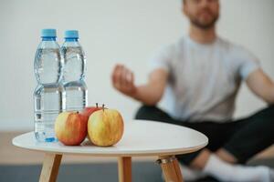 Bottles ,of water and apples. Yoga man is sitting on a mat at home photo