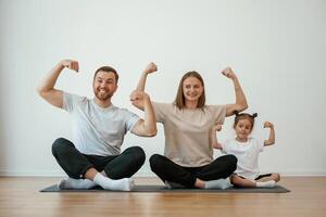 Showing, the ,biceps, strong.. Family of mother, father and daughter are doing yoga at home photo