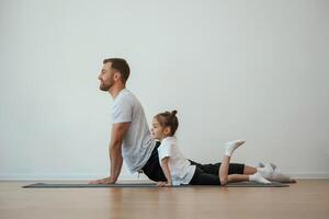 Against,, white wall, stretching. Father with little daughter are doing yoga at home photo