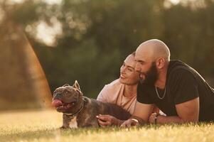 Calm, lying down on the ground... Man and woman are with dog on the field photo