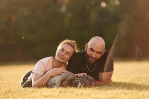 Calm, lying down on the ground. Man ,and, woman are with dog on the field photo