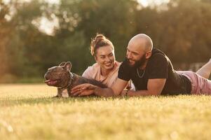 Calm, lying down on the ground., Man, and woman are with dog on the field photo