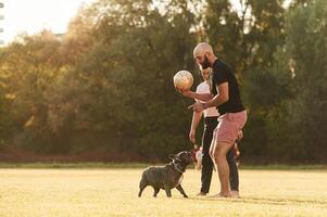 Using ,soccer, ball, playing. Man and woman are with dog on the field photo