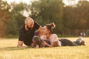 Positive facial expression, resting. Man and woman are with dog on the field photo