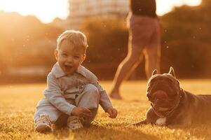 Smiling, little ,,boy is sitting with cute dog while father is walking on the summer field behind photo