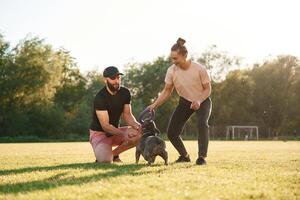 Active time spending, with rubber toy... Man and woman are with dog on the field photo