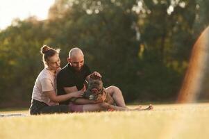 Weekend time, resting and sitting... Man and woman are with dog on the field photo
