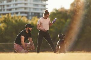 Playing ,with, a rubber toy. Man and woman are with dog on the field photo