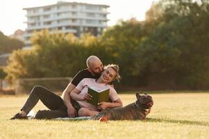 Weekend time, resting ,and, sitting. Man and woman are with dog on the field photo
