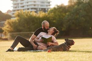 Weekend time, resting, and sitting. Man and woman are with dog on the field photo