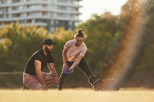 Playing with a rubber toy.. Man and woman are with dog on the field photo