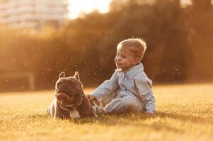 Sitting on the ground. Cute little boy ,is with dog on the field photo