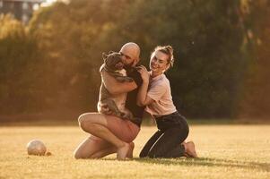 Positive facial expression,,, resting. Man and woman are with dog on the field photo