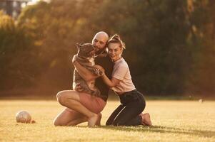 Positive facial expression, resting... Man, and woman are with dog on the field photo
