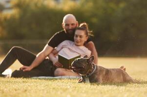 Weekend, time, resting and sitting. Man and woman are with dog on the field photo