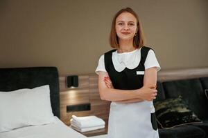 With arms ,crossed,, standing. Young chambermaid is in hotel room photo