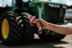 Close-up of hand holding wrench in, front of tractor photo