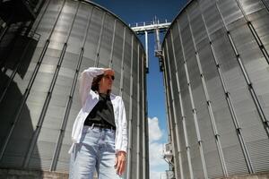 Looking, far away. Confident worker standing in front of industrial silos under clear blue sky photo