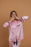 Front view, in pink pajama, waking up. Young pretty woman is against background in the studio. photo