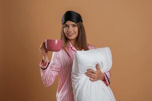 Conception of sleep products... With cup and pillow. Young pretty woman is against background in the studio photo