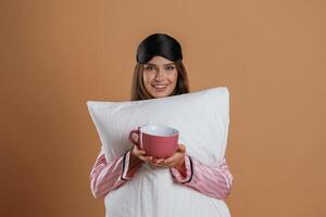 Conception of ,sleep products. With cup and pillow. Young pretty woman is against background in the studio photo