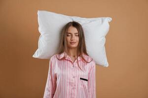Lying, down on the pillow, in pajama. Young pretty woman is against background in the studio photo