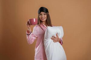 Conception of sleep products.. With cup and pillow. Young pretty woman is against background in the studio photo