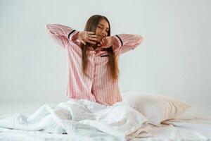 Front ,view, in pink pajama, waking up. Young pretty woman is against background in the studio photo