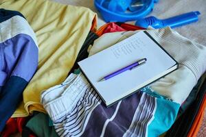 Preparing for travel, packing clothes in suitcase with checklist photo