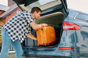 Man preparing for journey, loading suitcase in car trunk. Male traveler loading luggage for road trip photo