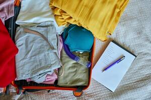Handwritten checklist and pen on clothes packed into suitcase. Preparing for travel. Holiday and vacation planning photo