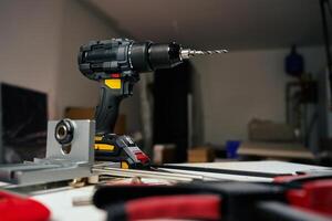 Electric cordless drill with bits and hand tools on workbench in workshop. Home renovation, construction and repair concept photo