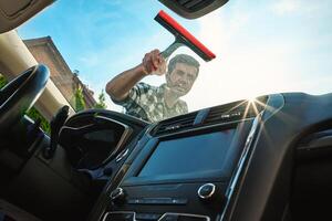 Man cleaning car windshield with squeegee, view from inside photo