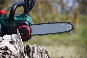 Close-up of a modern electric chainsaw resting near a tree stump in a natural setting. photo