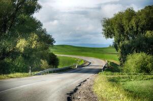 A beautiful winding road leading to a bright, green field on a sunny day in the countryside. photo