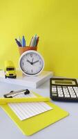 Vibrant Workspace with Clock and Stationery A vibrant workspace setup featuring a yellow background. Items include a white clock, colorful pens in a pot, a yellow toy truck, a calculator, and notepads video