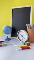 brilhante e alegre área de trabalho com quadro-negro e papelaria colorida escola suprimentos arranjo com papel clipes colorida educacional área de trabalho com globo e relógio video